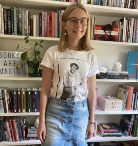 Agnes Lindholm står framför en bokhylla iklädd en t-shirt med Astrid Lindgren-tryck.