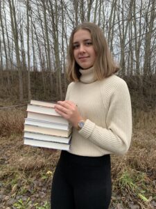 Alexandra Andersson står utomhus med en trave böcker i händerna.