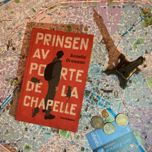 Boken "Prinsen av Porte de la Chapelle" ligger på en karta av Paris. Bredvid ligger några euro och ett metrokort. Ett litet Eiffeltorn står också på kartan.