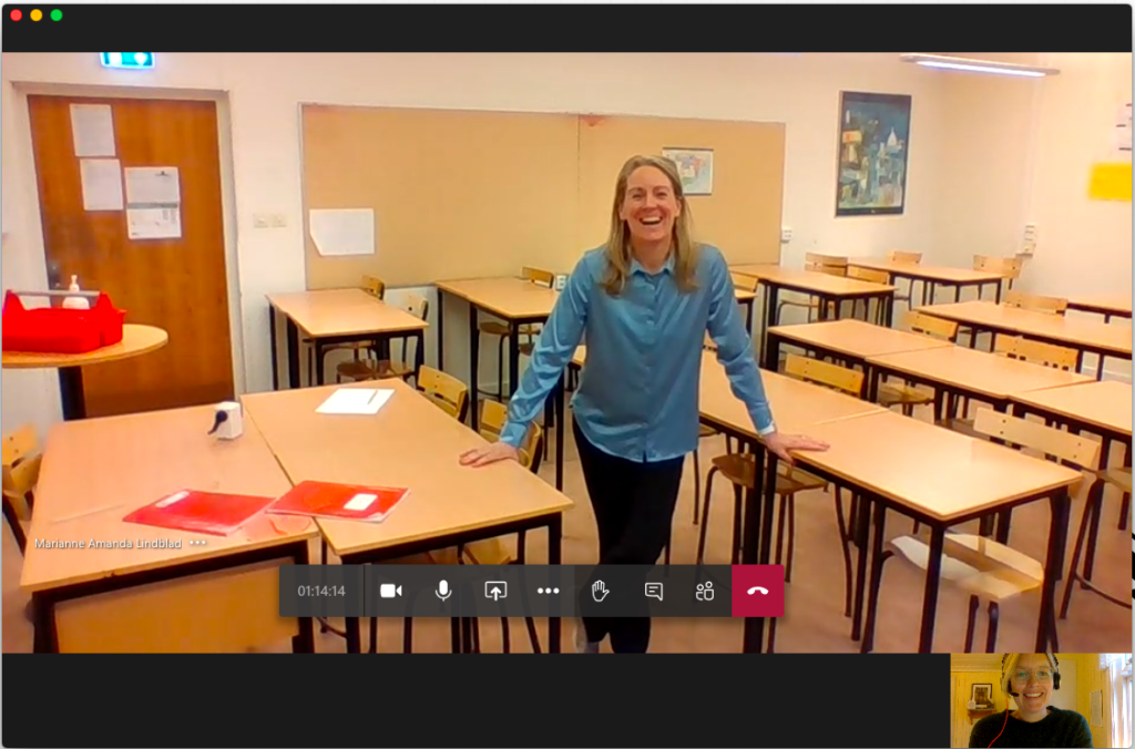 En lärare i ett tomt klassrum på en stor videobild, samt Annelie Drewsen med hörlurar på en mindre videobild. Skärmdump från videomöte. 